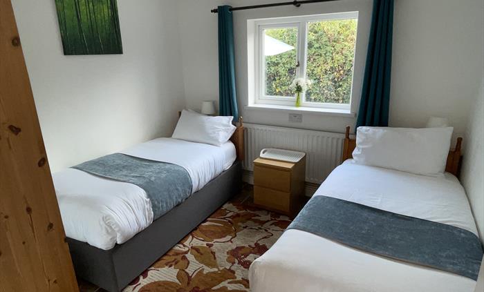 Twin bedroom with 2 full size single beds, 2 bedside cabinets, mirror wardrobe and window overlooking the private garden area
